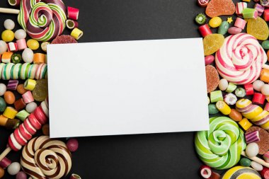 siyah arka plan üzerinde lezzetli çok renkli tatlılar ve boş beyaz kart üst görünümü