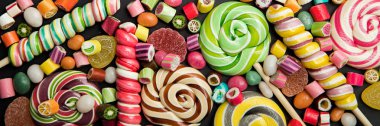 panoramic shot of bright round and swirl lollipops among fruit caramel candies clipart