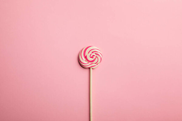 вид сверху на вкусный разноцветный вихревой леденец на деревянной палочке на розовом фоне
