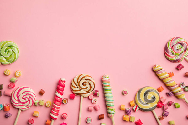 top view of delicious multicolored swirl lollipops on wooden sticks and candies on pink background