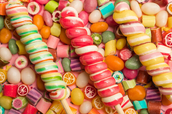 вид сверху на яркие вкусные разноцветные карамельные конфеты и вихревые леденцы на деревянных палочках
