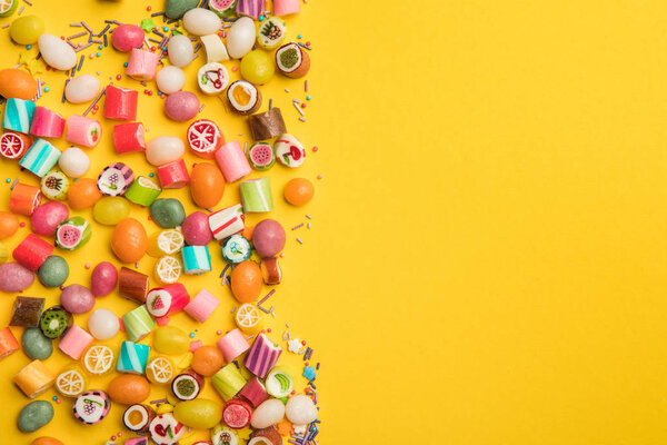 top view of multicolored candies and sprinkles scattered on yellow background with copy space