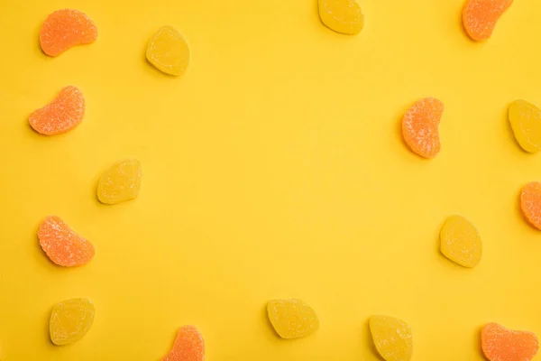 黄色の背景に散らばったおいしいオレンジとレモンゼリーのトップビュー — ストック写真