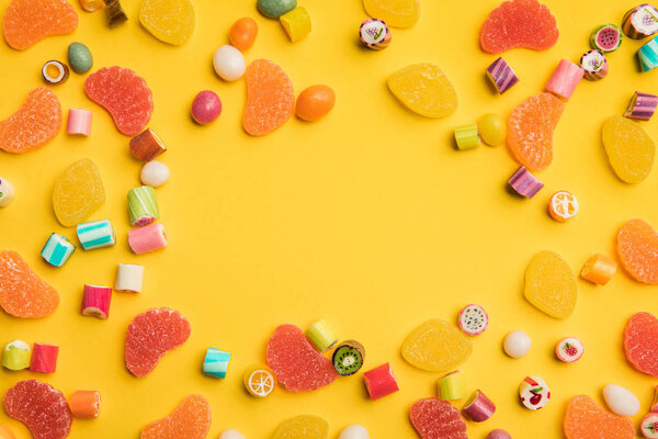 top view of multicolored tasty caramel and fruit jelly candies scattered on yellow background with copy space