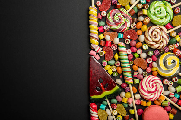 top view of delicious multicolored sweets on black background 