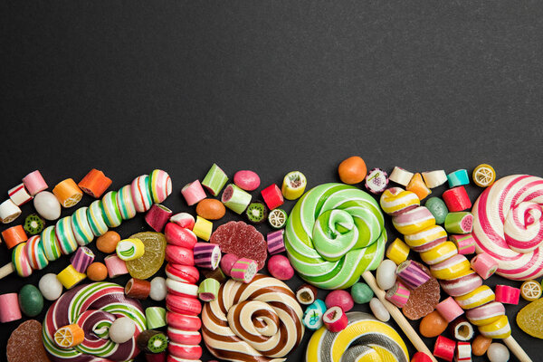 top view of tasty multicolored caramel sweets and lollipops on black background with copy space
