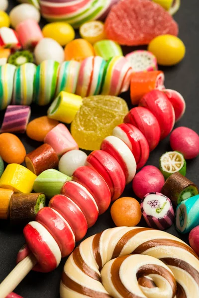 フルーツキャラメル多色キャンディーの間の明るい渦巻きロリポップのクローズアップビュー — ストック写真