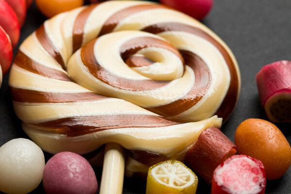 close up view of lollipop among caramel multicolored candies on black background