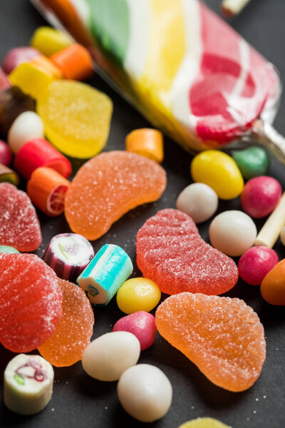 selective focus of delicious multicolored caramel and jelly sweets on black background