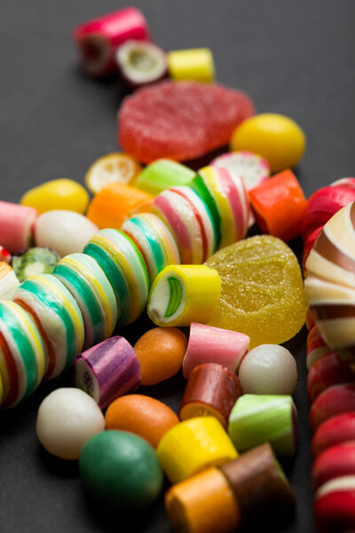 selective focus of delicious multicolored caramel and jelly candies on black background