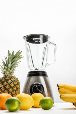 low angle view of blender near yellow bananas, ripe pineapple, lemons, orange and limes on white  clipart