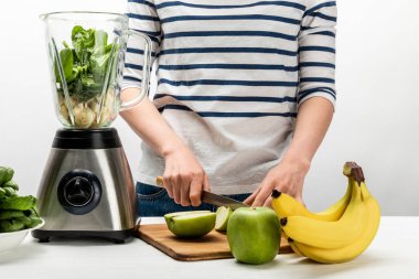 cropped view of woman cutting apple near blender and bananas on white  clipart