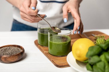 gri yeşil taze smoothie gözlük yanında chia tohumu ile kaşık tutan kadın kırpılmış görünümü 