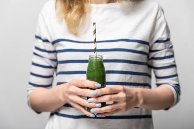 beyaz lezzetli yeşil smoothie ve saman ile cam şişe tutan kadın kırpılmış görünümü 