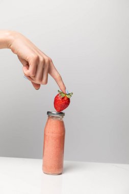 gri lezzetli pembe smoothie ile cam şişe yakınında olgun çilek tutan kadın kırpılmış görünümü 
