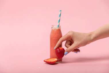 pembe lezzetli smoothie ile cam şişe yakınında olgun çilek tutan kadın kırpılmış görünümü 