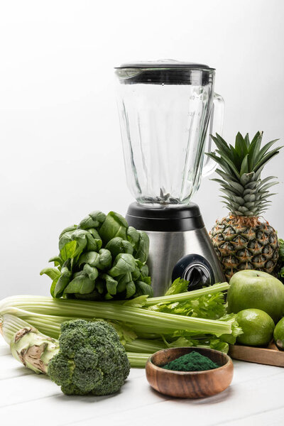 blender near fresh, green vegetables and organic fruits on white 