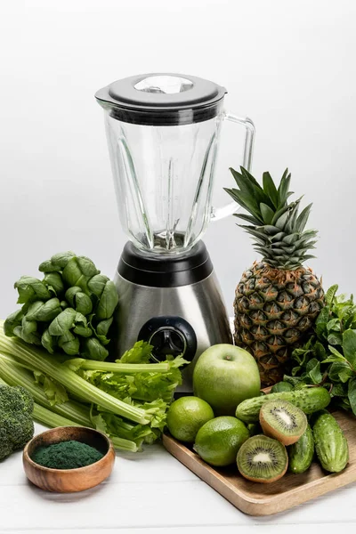 blender near fresh, green vegetables and organic raw fruits on white