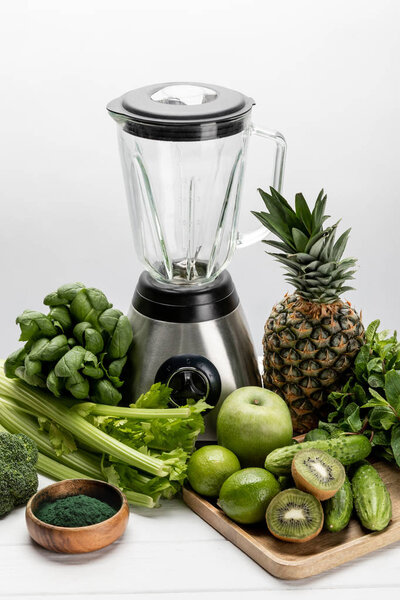 blender near fresh, green vegetables and organic raw fruits on white 