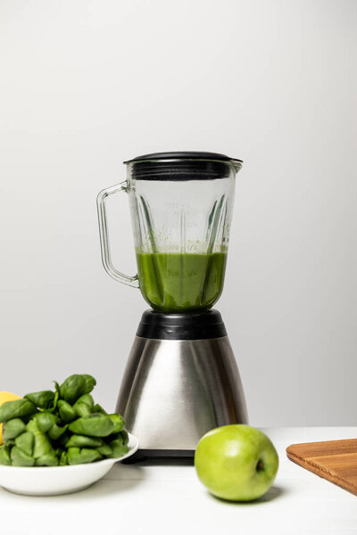 green tasty apple near spinach leaves and blender on grey 