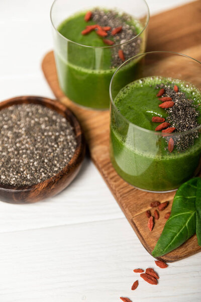 tasty green smoothie in glasses with chia seeds and goji berries on white surface 