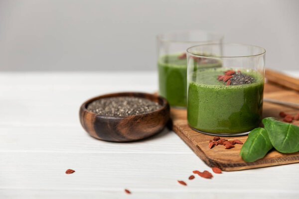 tasty green smoothie in glasses with chia seeds and goji berries on grey