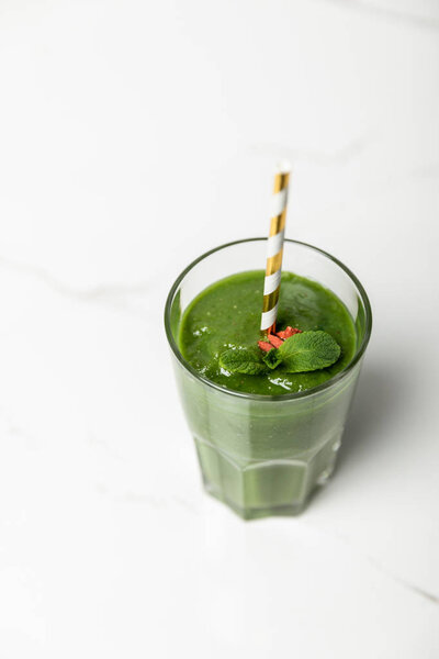overhead view of green, organic smoothie with goji berries and mint in glass with straw on white 