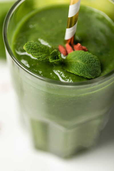 close up of green smoothie with goji berries and mint in glass with straw on white 