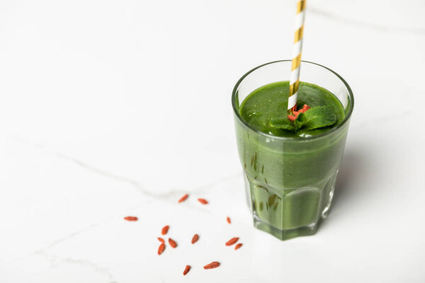 selective focus of tasty smoothie with goji berries and mint in glass with straw on white 