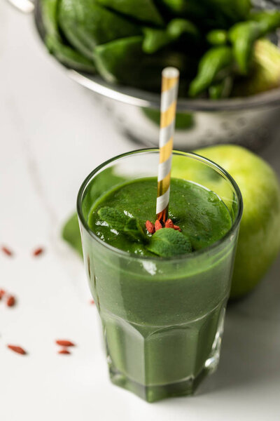 selective focus of tasty smoothie in glass with straw near spinach leaves and apple on white 