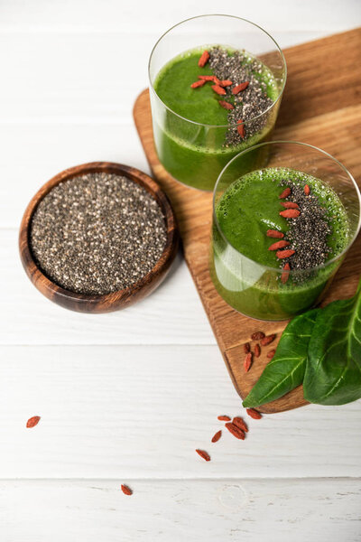 top view of chia seeds in bowl near glasses of green smoothie on white 