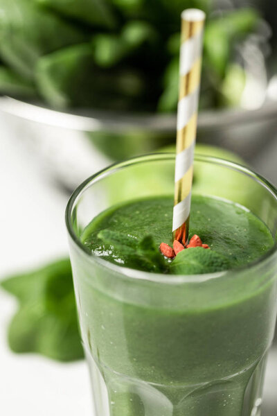selective focus of tasty green smoothie in glass with straw near spinach leaves on white 