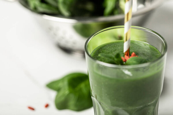 selective focus of tasty green smoothie in glass with straw near fresh spinach leaves on white 