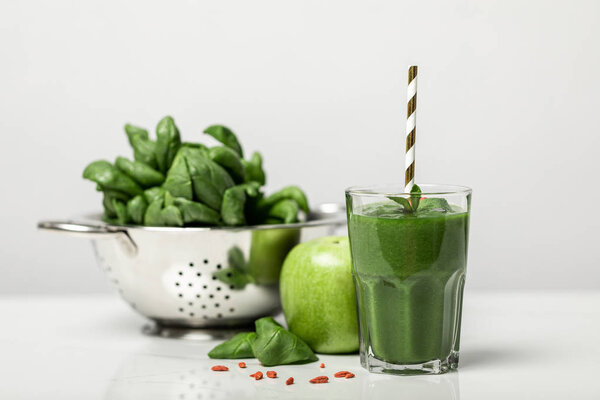 селективный фокус зеленого смузи в стекле с соломой возле листьев шпината и яблоко на белом
 