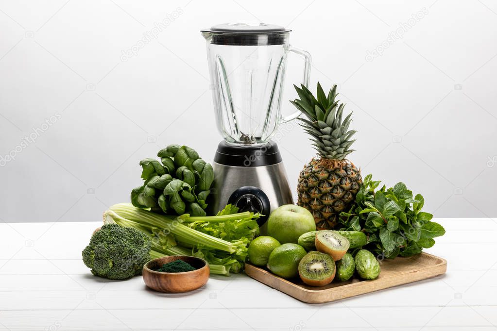 blender near green fresh vegetables and tasty fruits on white 