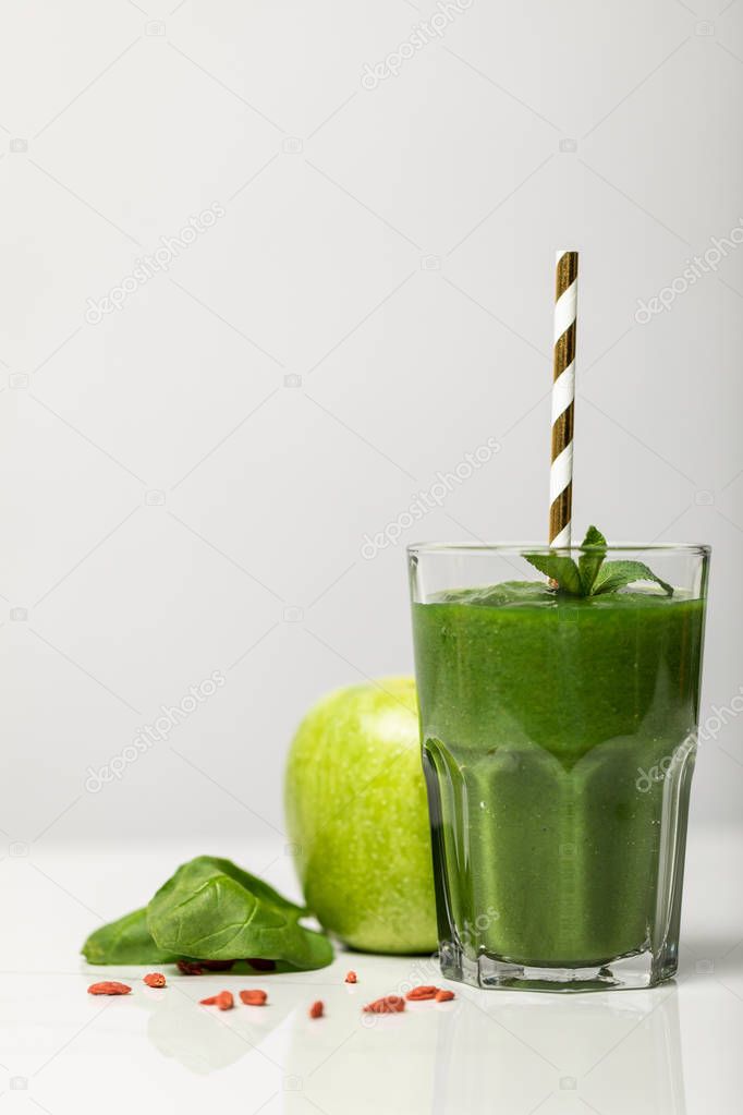 green smoothie in glass with straw near ripe organic apple on grey 