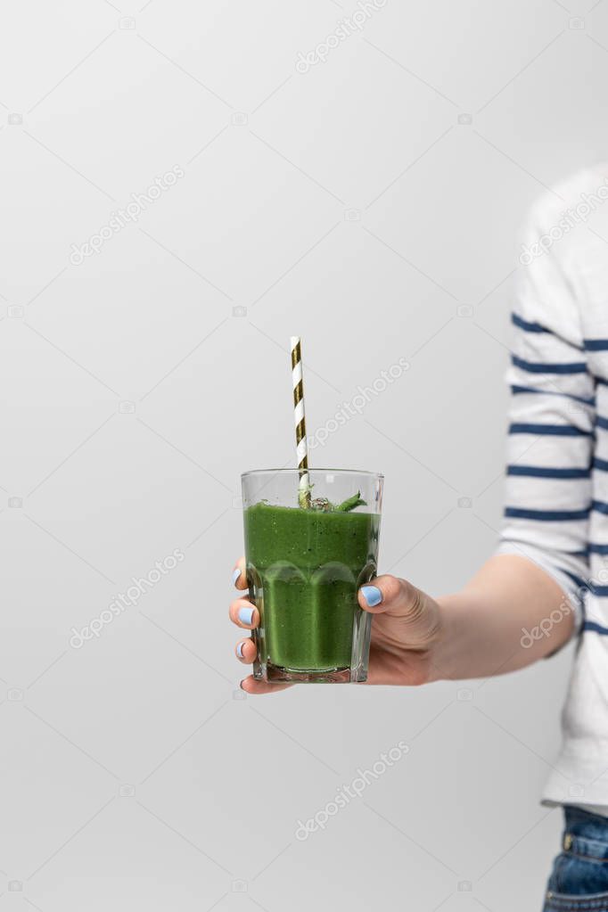 cropped view of woman holding glass with tasty green smoothie and straw on white 