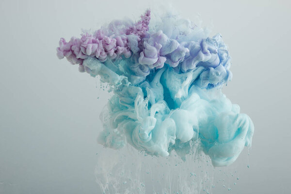 Close up view of light blue, pink and purple paint mixing isolated on grey