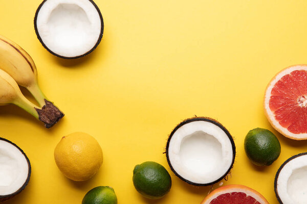 top view of citrus fruits, bananas and coconuts on yellow background with copy space