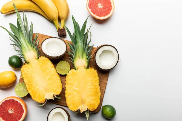top view of cut and whole exotic fruits on wooden chopping board on white background