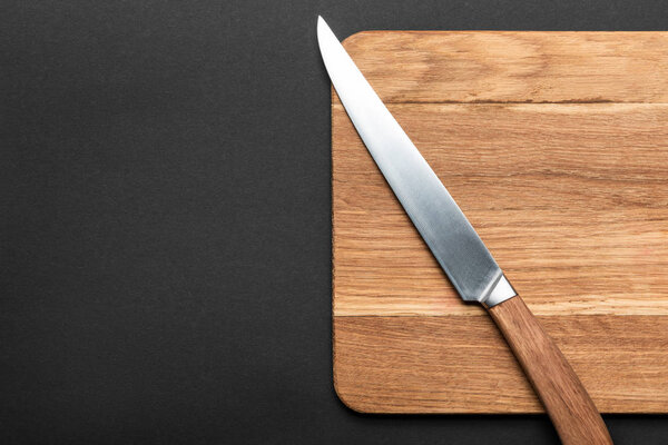 top view of knife and wooden cutting board on black background