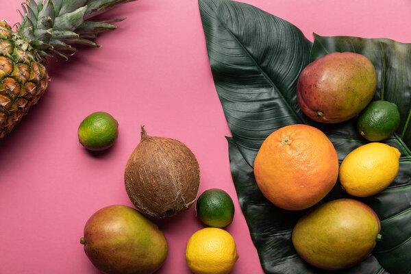 верхний вид спелых тропических ярких фруктов с зелеными листьями на розовом фоне
 