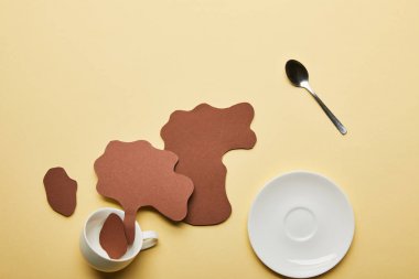 top view of paper cut coffee spills near white cup, saucer and spoon on beige background clipart