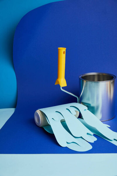 empty shiny can near roller with dripping paper cut paint on bright blue background