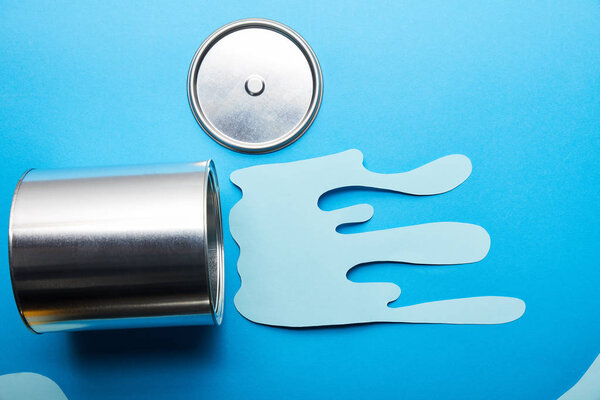 top view of metal shiny can and can near dripping paper cut paint on bright blue background