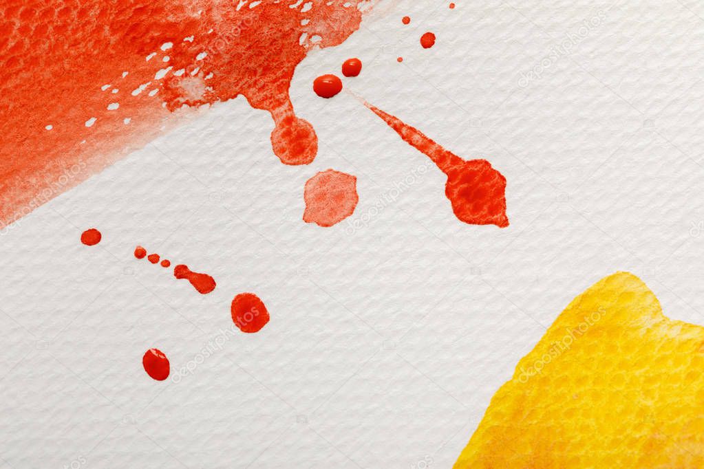 close up view of yellow and red watercolor paint brushstrokes with drops on white textured background