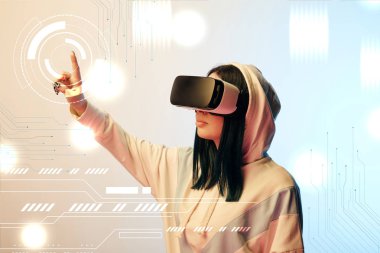 young woman in virtual reality headset pointing with finger at glowing cyber illustration on beige and blue background clipart