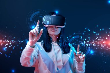 woman in virtual reality headset pointing with fingers at glowing cyber illustration on dark background clipart