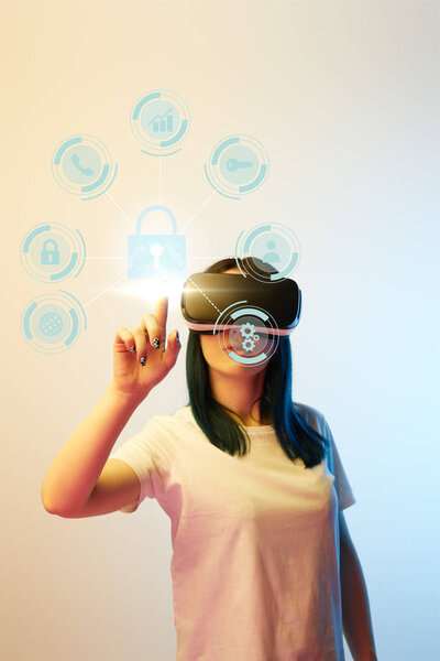 young woman in virtual reality headset pointing with finger at internet security icons on beige and blue background