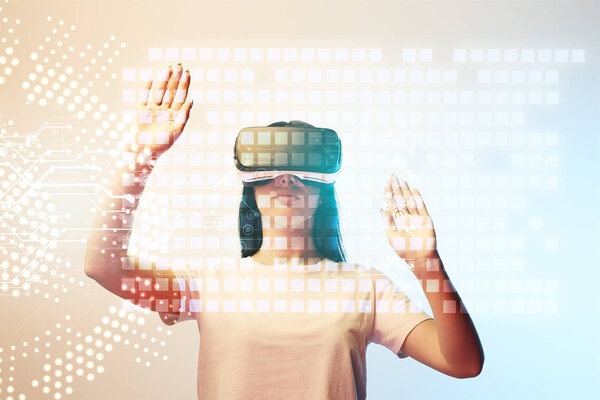 young woman in virtual reality headset pointing with hands at glowing data illustration on beige and blue background
